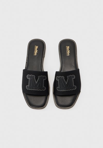 Sorte sandaler i svart med overdel i teksturert stoff som har brodert "M"-logo. Designet inkluderer en glatt lærinnersåle og kontrasterende sømmer.