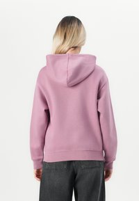 Roze hoodie met een zachte textuur, voorzien van een grote capuchon, geribbelde mouwen en tailleband, gecombineerd met donkergrijze wijde jeans.