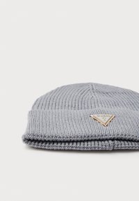 Căciulă tricotată ribbed de culoare gri deschis, cu margine pliată și un logo metalic triangular Guess aproape de tiv.