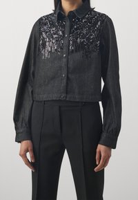 Camicia nera in denim tagliata, caratterizzata da una parte superiore decorata con paillettes, chiusura con bottoni e maniche lunghe con polsini abbottonati.
