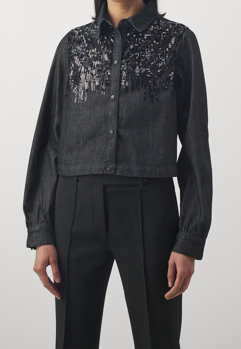 Camicia nera in denim tagliata, caratterizzata da una parte superiore decorata con paillettes, chiusura con bottoni e maniche lunghe con polsini abbottonati.