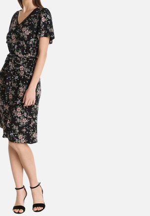 Zwart bloemenjurk met een V-hals, korte mouwen en een getailleerde taille. Heeft roze en witte bloemenpatronen; gecombineerd met zwarte hoge hakken sandalen.