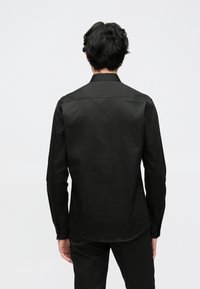 Zwart lang mouw shirt met een gladde textuur, klassieke kraag en knoopmanchetten, voorzien van een getailleerde pasvorm en achterkant met inzetstuk.