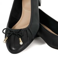 Zwarte leren ballerina's met een ronde neus, gestikte plooien, een decoratieve strik met gouden accenten en parelachtige kralen. Glad van textuur.