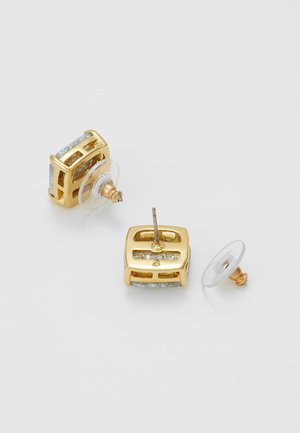 Goldene quadratische Ohrstecker mit irisierenden Einsätzen, einer mit abgelöstem klarem Plastikverschluss, auf einer weißen Oberfläche dargestellt.