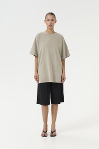 Oversized beige cotton t-shirt with short sleeves, paired with black knee-length shorts. Simple design, no visible patterns or embellishments.