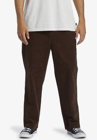 Brown corduroy pants with straight legs, textured fabric, and side pockets, paired with black and white sneakers.