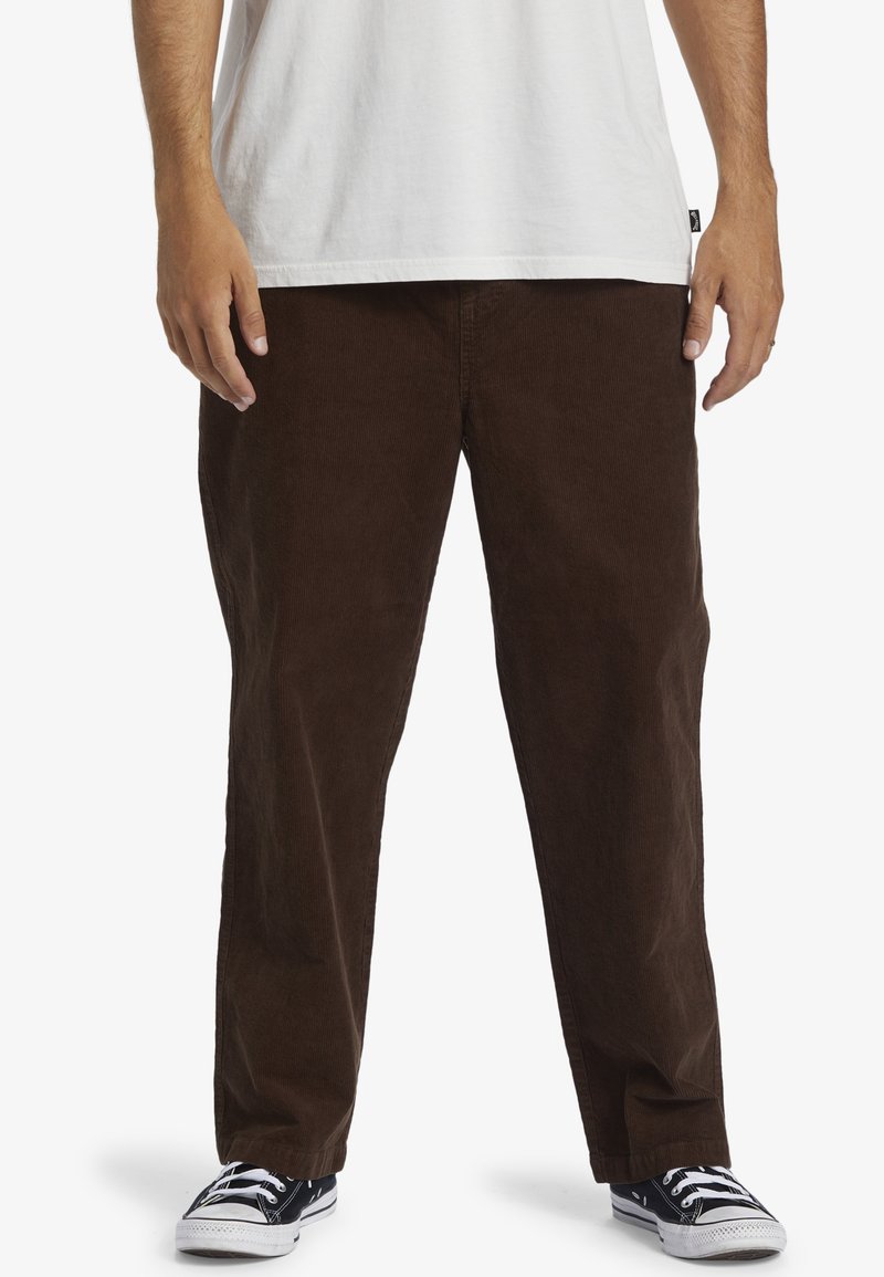 Brown corduroy pants with straight legs, textured fabric, and side pockets, paired with black and white sneakers.