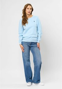 Ljusblå sweatshirt med ribbade ärmar och rundad halsringning, kombinerad med vida blå denimjeans och vita sneakers.