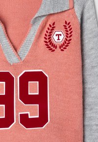Maglione lavorato a maglia rosa e grigio con scollatura a V, caratterizzato da un grande "99" rosso e un emblema con foglie di alloro e un logo esagonale.