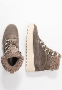 Bottes en suede marron avec un col en fourrure douce, des œillets en métal et une semelle crême dentelée. Présente une finition texturée et un design superposé.