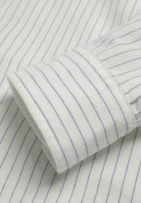 Puño de camisa de tela blanca con finas rayas azules, que presenta una textura suave y costuras limpias a lo largo de los bordes.