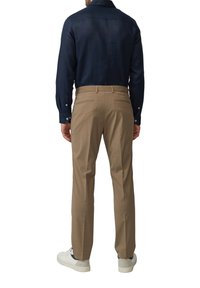 Navy langesleeve shirt met knoopsluiting bij de mouwen, gecombineerd met lichtbruine op maat gemaakte broeken en witte sneakers, gezien vanaf de achterkant.