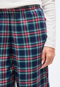 Παντελόνι lounge με καρό σε ναυτικό μπλε, πράσινο και κόκκινο. Διαθέτει ελαστική μέση και απαλό ύφασμα με βουρτσισμένη υφή. Χέρι ορατό στο πλάι.