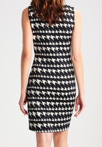 Sukienka w czarno-białą kratę houndstooth, dopasowana, bez rękawów, o długości do kolan, wykonana z gładkiego, elastycznego materiału.