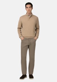 Beige knit sweater with a half-zip collar, paired with light brown pants and dark suede slip-on shoes. Minimalist design.