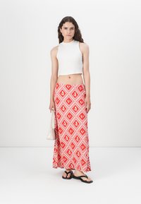 Top blanco cropped sin mangas, falda maxi roja con un patrón de diamantes blancos, chanclas negras y bolso beige. Textura de tela suave.