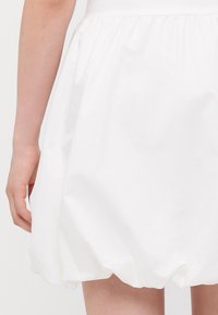 Weißer Baumwollrock mit elastischem Bund, der ein voluminöses, gerüschtes Design und eine glatte, leichte Textur aufweist.