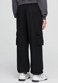 Pantaloni cargo neri con una vestibilità comoda, dotati di tasche laterali e cintura elastica. Indossati con sneakers bianche per un contrasto.