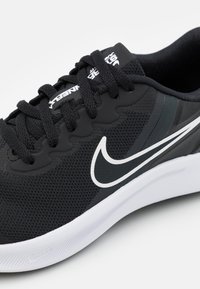 Scarpa da ginnastica nera con tomaia in rete, dotata di un logo Nike bianco a contrasto, lacci testurizzati e una suola bianca elegante e curva.