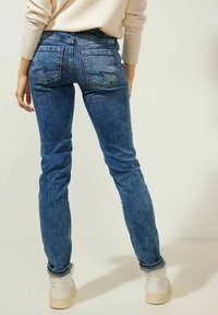 Jeans skinny de mezclilla azul con un lavado desgastado, cinco bolsillos y costuras visibles. Combinados con zapatos blancos, los jeans tienen un ajuste ceñido.