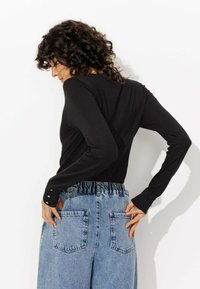 Haut noir à manches longues avec un design ajusté, affichant des accents de bouton aux poignets, associé à un pantalon en denim bleu clair taille haute.