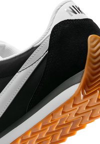 Baskets noir et blanc avec un dessus en maille, des accents en daim et une semelle extérieure en caoutchouc orange texturé avec un motif en zigzag.