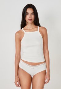 Top in cotone chiaro a coste con spalline sottili, abbinato a pantaloni boyshort coordinati con bordo in pizzo e un piccolo dettaglio a fiocco.