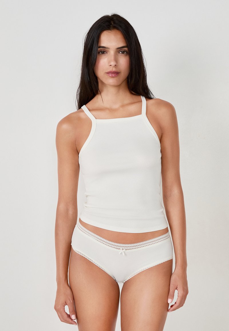 Top in cotone chiaro a coste con spalline sottili, abbinato a pantaloni boyshort coordinati con bordo in pizzo e un piccolo dettaglio a fiocco.