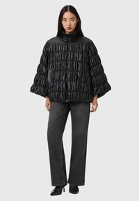 Svart vadderad jacka med samlad textur, hög krage och dragkedja, kombinerad med mörka vida jeans och spetsiga svarta klackar.