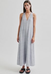 Rochie lungă, gri, cu bretele halter și decolteu adânc în V, cu un model în carouri. Fabricată dintr-un material ușor, având o siluetă fluidă și fente laterale.