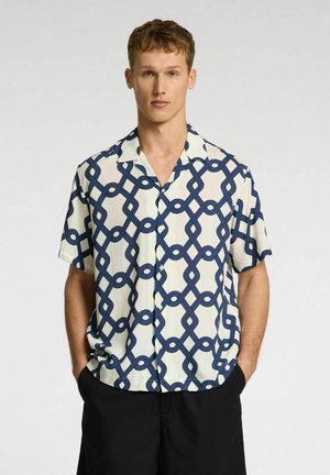 Chemise à manches courtes en tissu crème avec un motif de chaîne liée bleu marine, dotée d'une fermeture à boutons et d'un col ouvert.