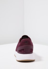 Burgundy athletic shoe with a suede upper, padded collar, black logo on heel, and white midsole. Textured rubber outsole for traction.