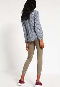 Chemise à manches longues florale en bleu et blanc, associée à un pantalon skinny beige et des chaussures enfilables prune. Tissu lisse et coupe ajustée.