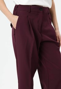 Bordeauxrode, op maat gemaakte broek met een gladde textuur, zijzakken en een knoopsluiting, uitgevoerd in een recht model met subtiele plooien.