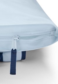 Geantă din material bleu deschis, cu un fermoar bleumarin și un tab de tragere texturat. Geanta are o suprafață netedă și un aspect subtil lucios, cu cusături vizibile.