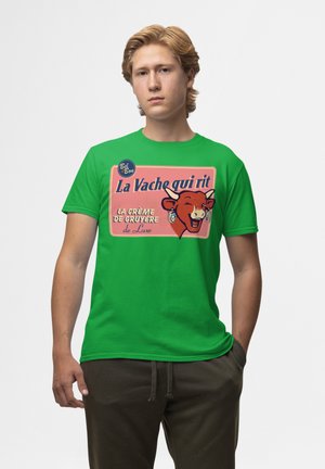 Grøn bomulds t-shirt med grafisk tryk af en smilende ko, med tekst på fransk: "La Vache qui rit" og "la crème de Gruyère."