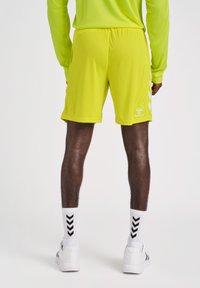 Neon-gelbe Sportshorts mit einem elastischen Bund, seitlichen Streifen und einem Logo am Unterschenkel, kombiniert mit weißen Socken und Schuhen.