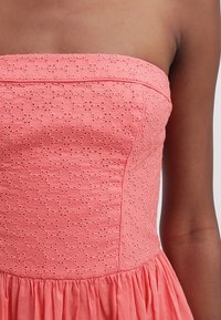 Korálově červené šaty bez ramínek se vyšívaným květinovým vzorem, texturovanou látkou a nařasenou sukní. Hladký živůtek s přiléhavým střihem.