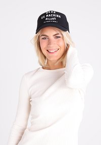 Cappellino da trucker nero con testo stampato bianco "DEUS EX MACHINA MILANO" e "VIA THAON DI RIVEL 3"; retro in rete, pannello frontale solido, visiera curva.