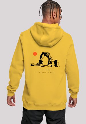 Gelber Kapuzenpullover mit einem Grafikdesign von einem Bogen und einer Sonne, darunter der Text "ENTFLIEHEN UND DIE WELT ENTDECKEN". Weiches Material, lockere Passform.
