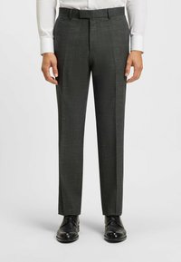 Pantaloni eleganti grigio scuro con un sottile motivo testurizzato, vestibilità dritta e passanti per cintura, abbinati a scarpe nere eleganti e una camicia bianca.