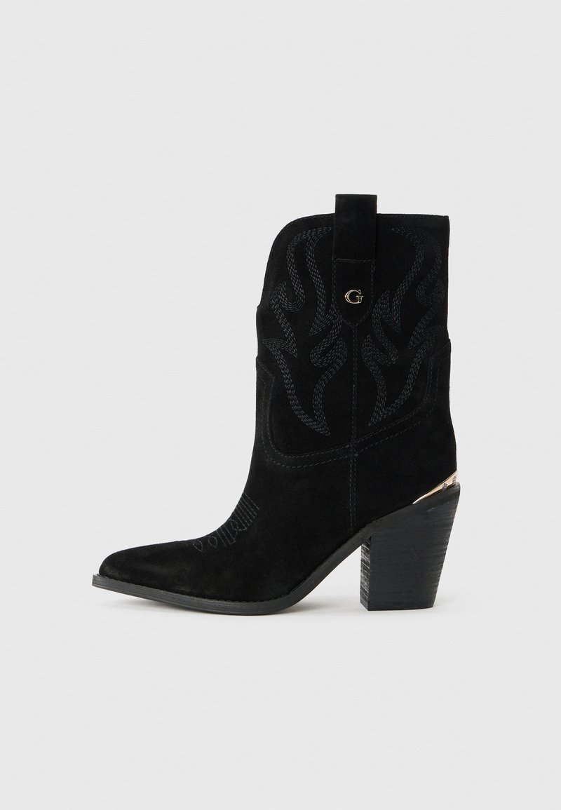 Bottines en suédine noire avec bouts pointus, portant des coutures décoratives, un logo doré et un talon en bloc en bois.