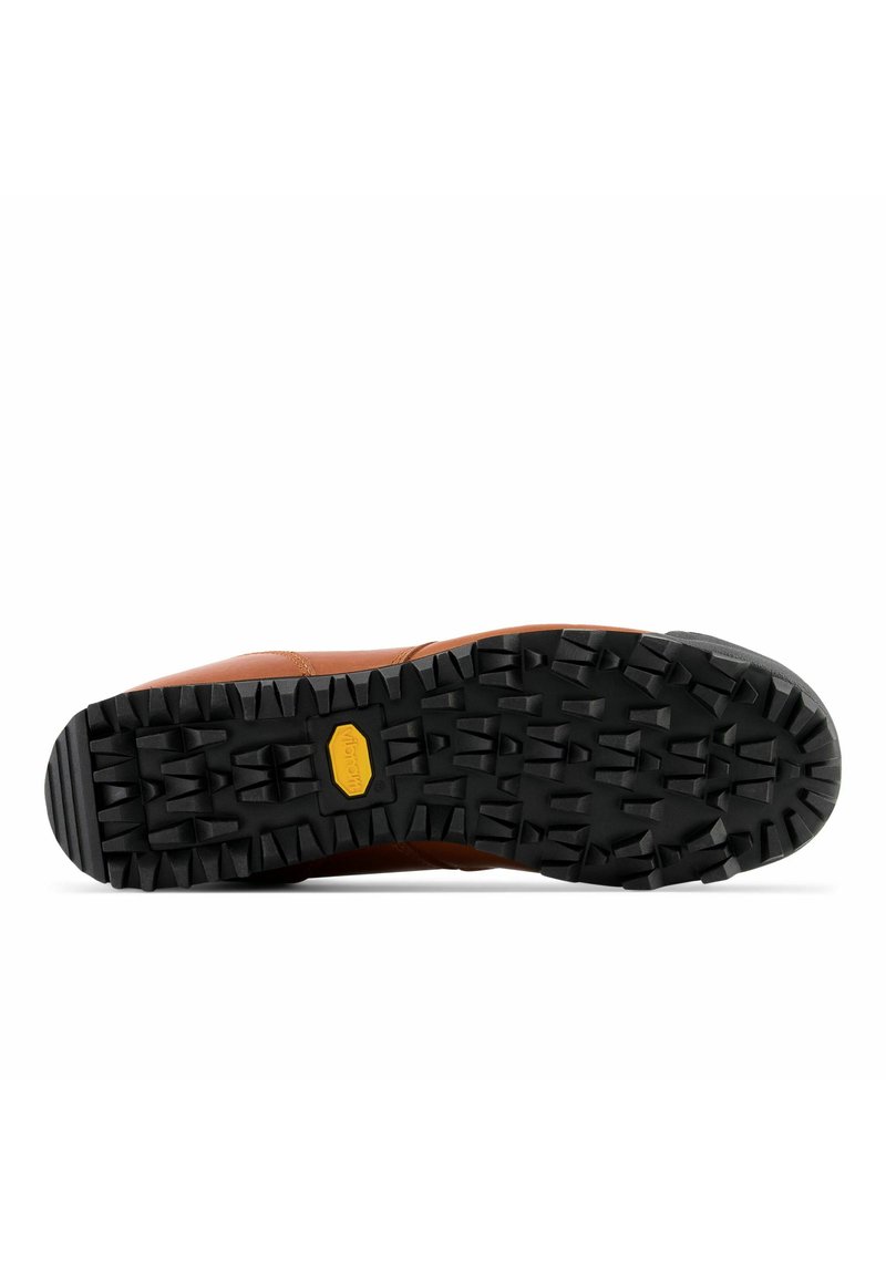 Chaussure en cuir marron avec une semelle en caoutchouc noir dotée de profondes rainures et d'un logo Vibram, conçue pour l'adhérence et la stabilité.