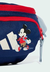Modrý látkový pásový vak s červenými akcenty, zdobený kreslenou postavičkou a bílým logem. Zipové uzávěr, nastavitelný popruh, odolný materiál.