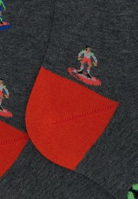 Calzini grigi con vivaci accenti rossi sul polsino e sulla punta, decorati da un motivo di figure colorate che surfa su tutta la stoffa.