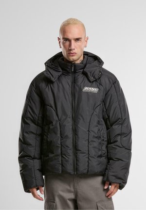 Veste noire rembourrée avec fermeture éclair, col montant et capuche ajustable. Présente des motifs cousus et un logo sur la poitrine.