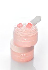 Maschera notturna al collagene Abib PDRN in un barattolo trasparente rosa, con coperchio bianco e una spatola all'interno, contiene gel con cubetti di gelatina rosa.