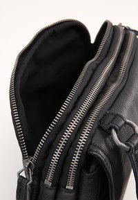 Svart läderväska med flera dragkedjefack, texturerad yta och metalldetaljer på dragkedjan. Inuti klädd i svart tyg.