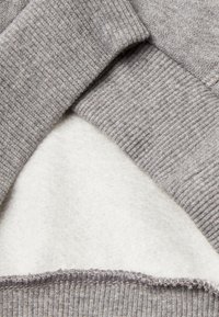 Tessuto grigio con un morbido interno in pile bianco. Presenta una texture a costine lungo i bordi. Include un design a strati con materiali a contrasto.
